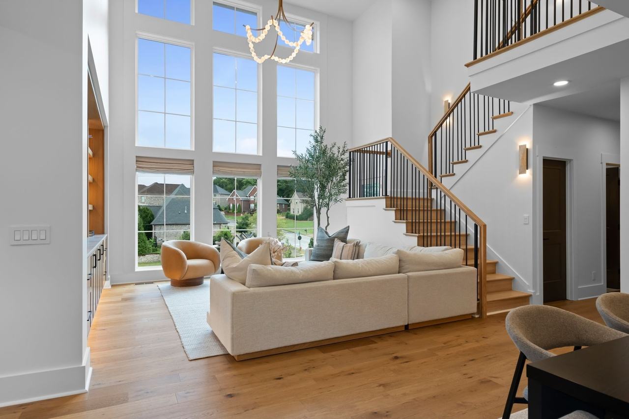 The living room toward the two-story wall of windows: two curved swivel chairs, an olive tree and Roman shades.