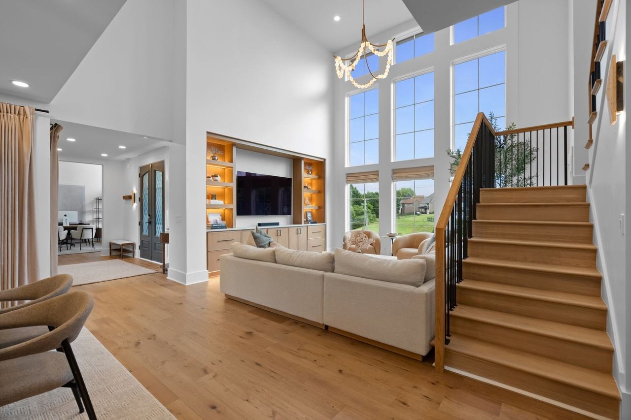 The living room toward the media wall and foyer, the stair rising beside the built-ins.