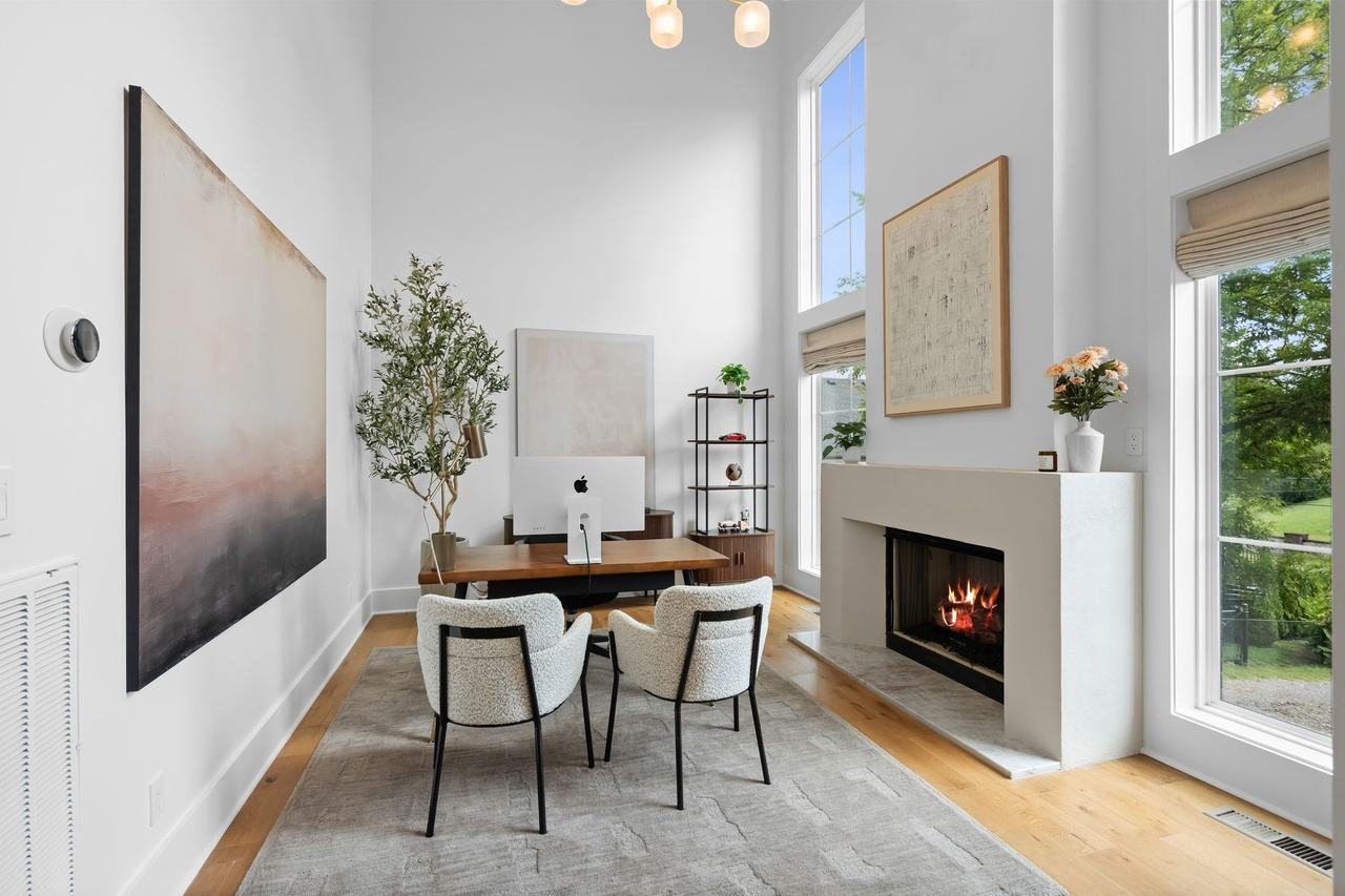 The office: a white plaster fireplace surround with a framed map above, a desk and two upholstered chairs on a gray rug.