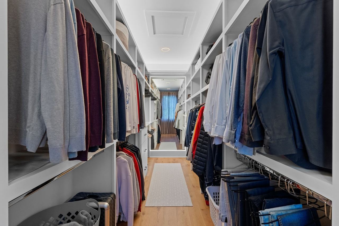 The original walk-in closet, white shelving and hanging rods on both sides, toward a full-length mirror.