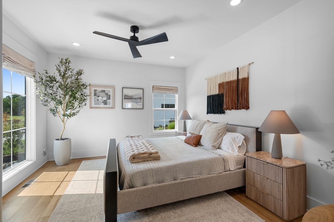 The downstairs guest bedroom from the corner: a woven wall hanging, a marble-topped nightstand and an olive tree by the window.