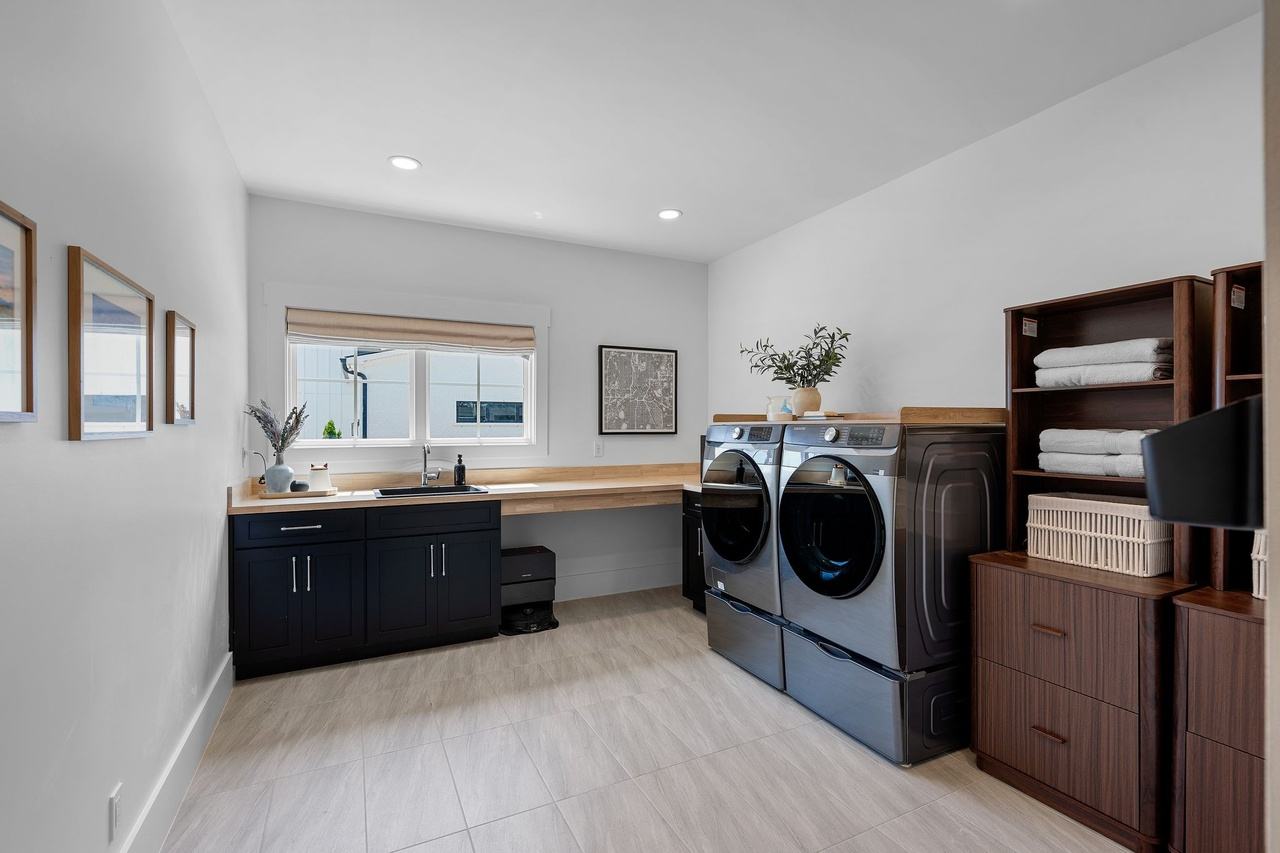 The laundry room: black cabinets and a butcher-block counter under the window, a washer and dryer on pedestals, walnut shelving.