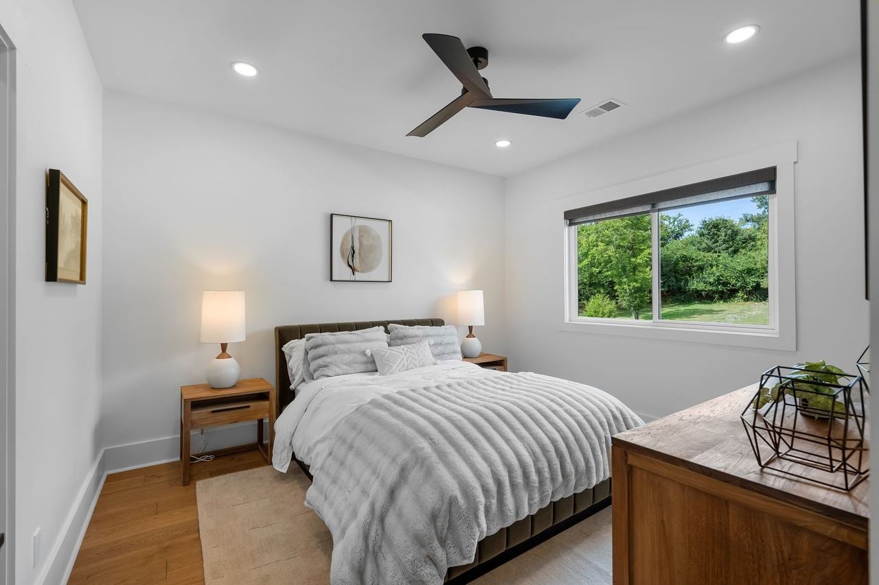 Guest room one: a bed between two nightstands under a round print, a window to the trees.