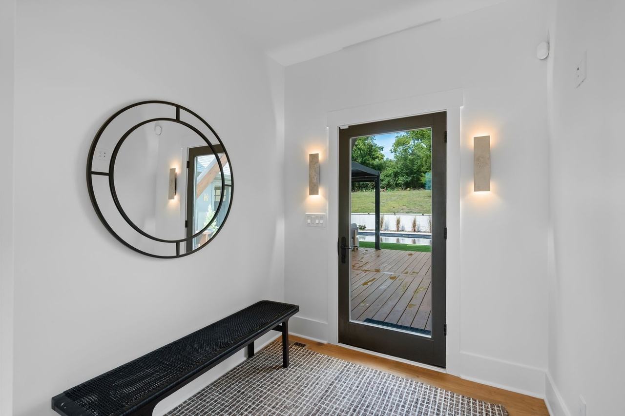 The back entry: a black bench, a round black mirror and two stone sconces beside the glass door to the deck.