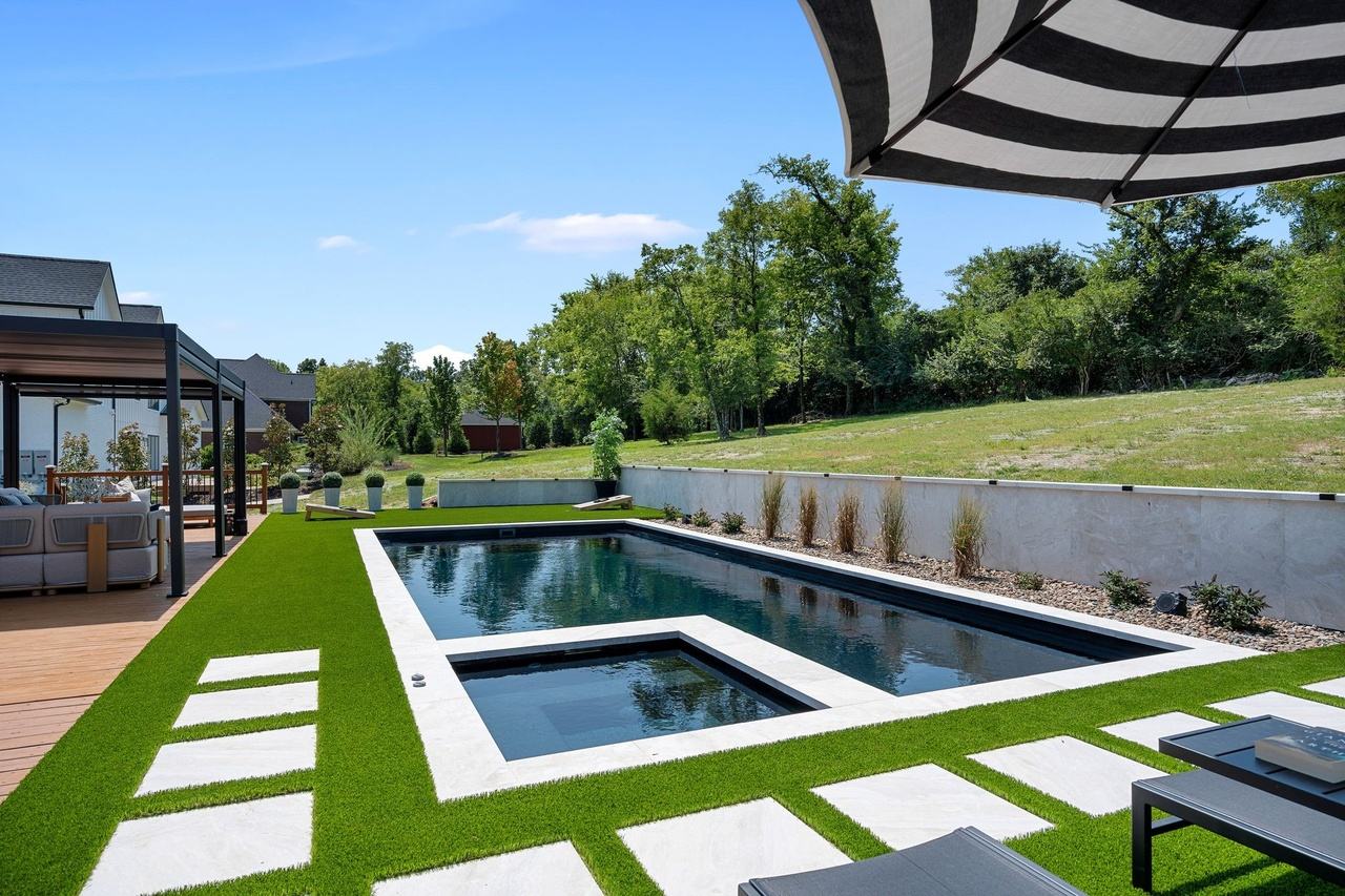The pool from the spa end, pavers stepping across the turf toward the pergola.