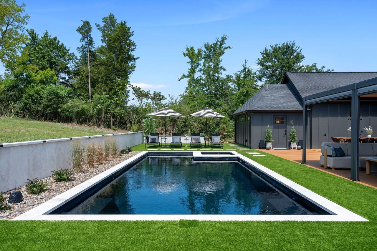 The pool from the far end toward four chaise loungers under striped umbrellas.