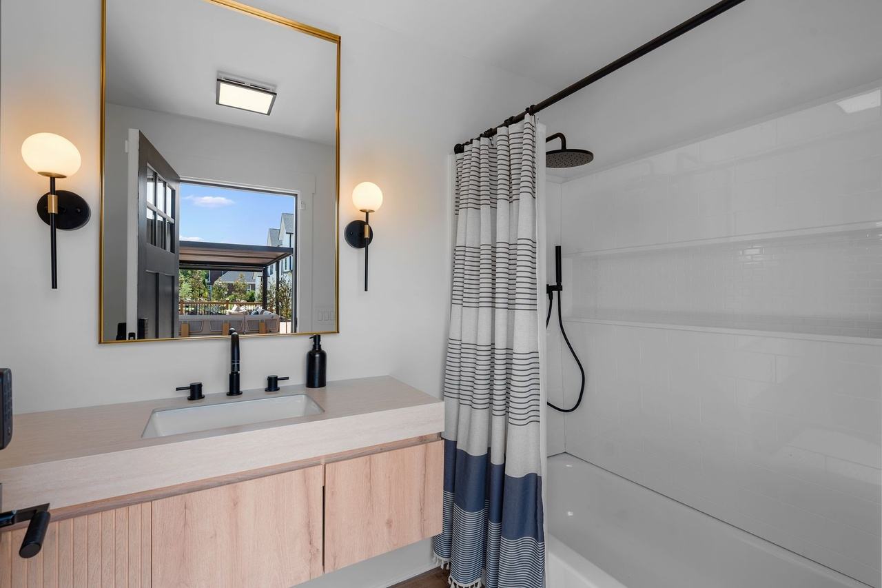 The pool bath: a pale wood vanity, a brass-framed mirror between black sconces, and a tub with a striped curtain.