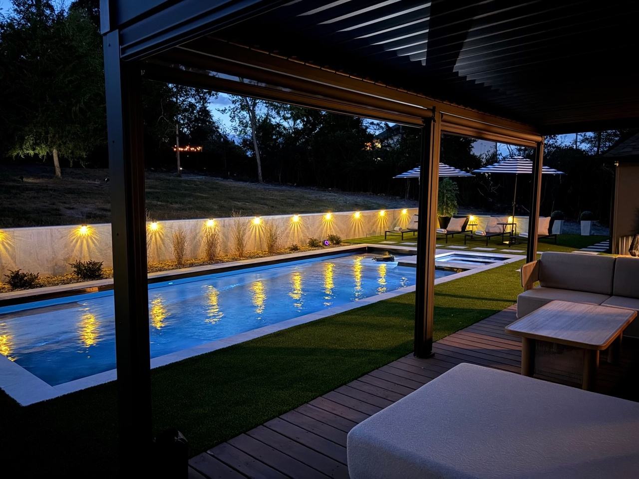 The pool at night from under the pergola, the retaining wall lights reflected in the water.