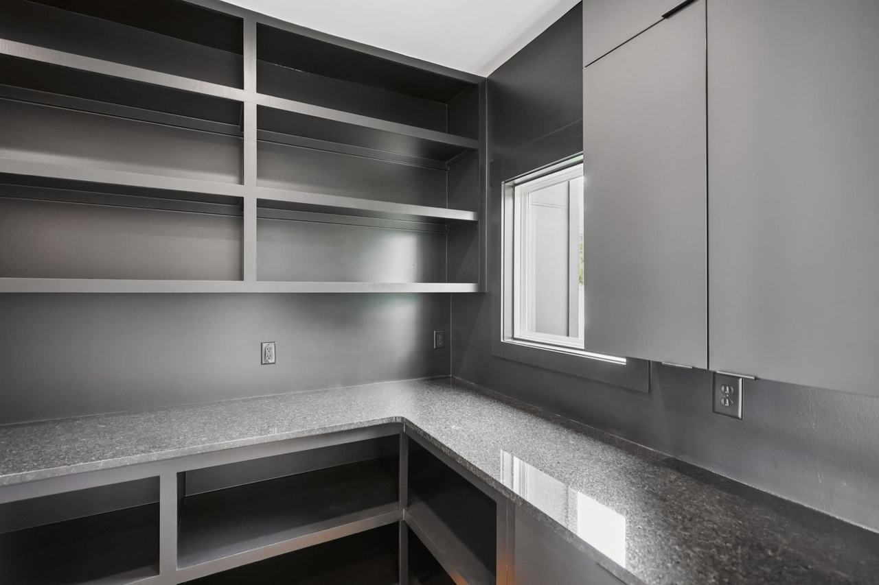 2025 photograph (before): Butlers Pantry, corner shelves under window, with dark built-in shelves, L-shaped granite counter, window