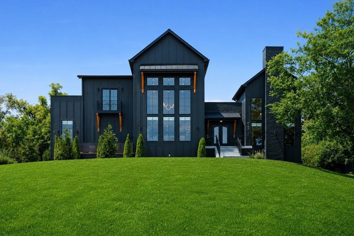 The front of the house straight on across the lawn, black board-and-batten with a tall grid of windows under the center gable.