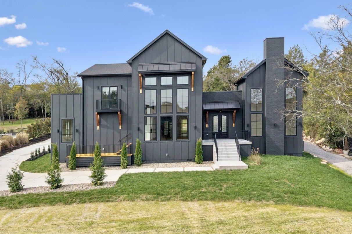 2025 photograph (before): Exterior Front, straight on in daylight, with board and batten, glass wall of windows, brick chimney, front steps