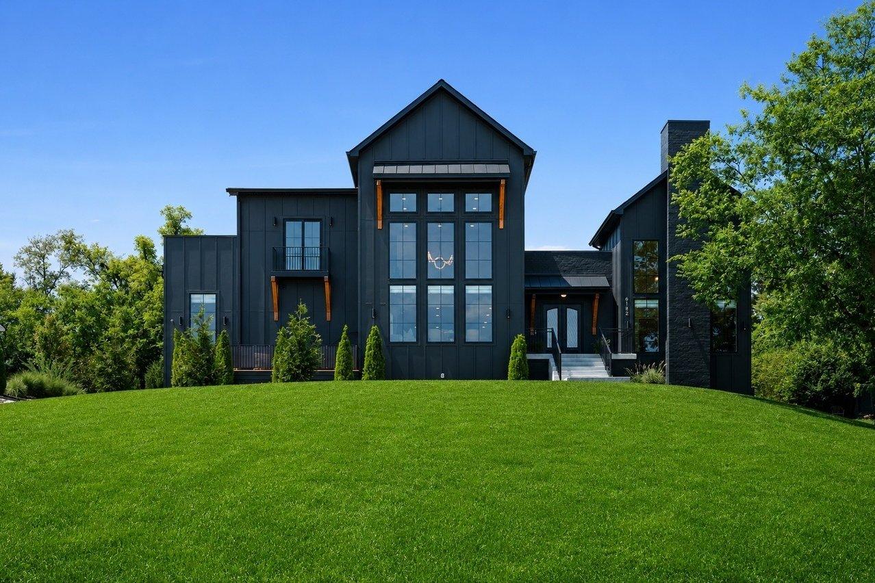 The front of the house straight on across the lawn, black board-and-batten with a tall grid of windows under the center gable.