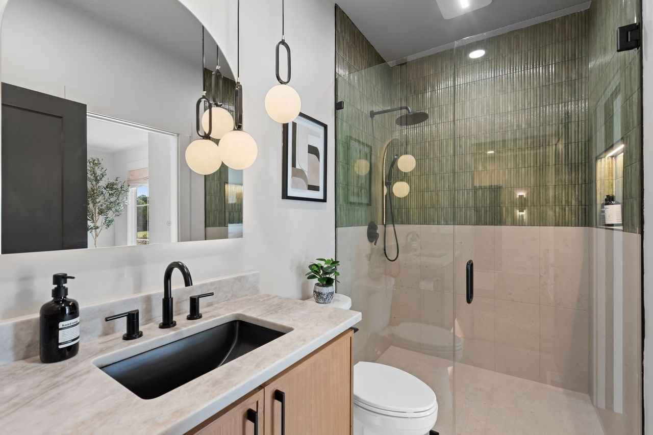 The guest bath: an oak vanity with a black undermount sink, globe pendants, and a shower in vertical green glazed tile.