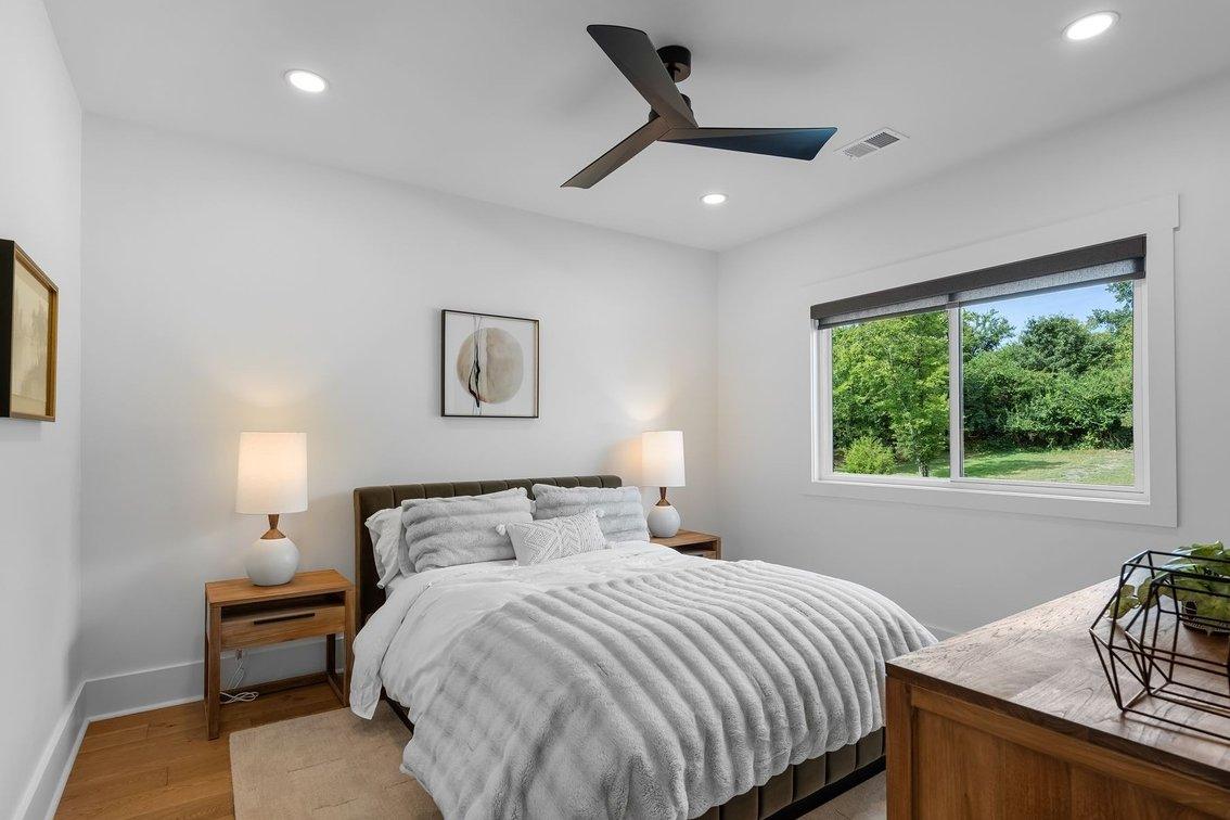 Guest room one: a bed between two nightstands under a round print, a window to the trees.