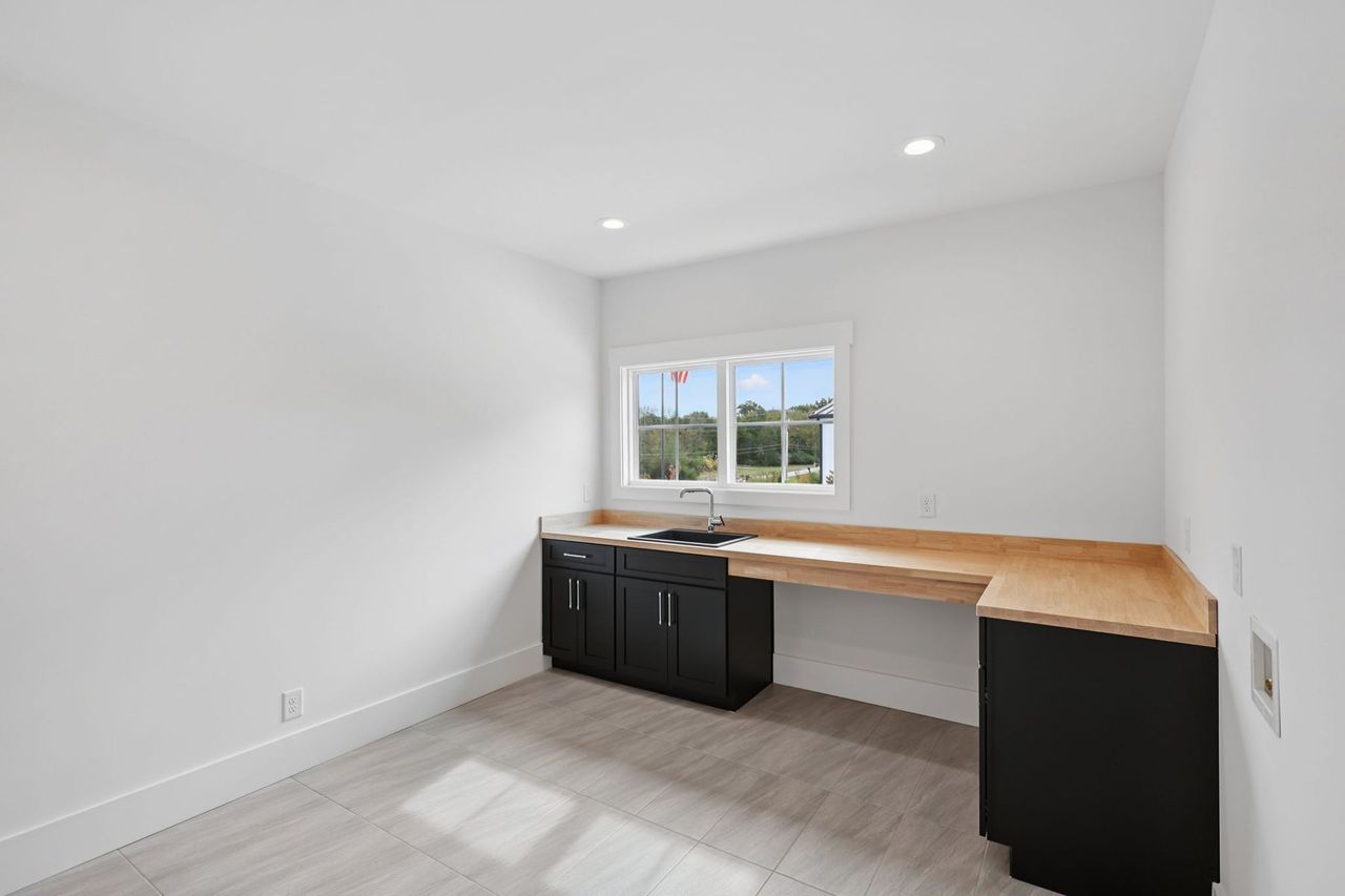 2025 photograph (before): Laundry Room, toward sink and wall of windows, with butcher block counter, black sink, black cabinets, window