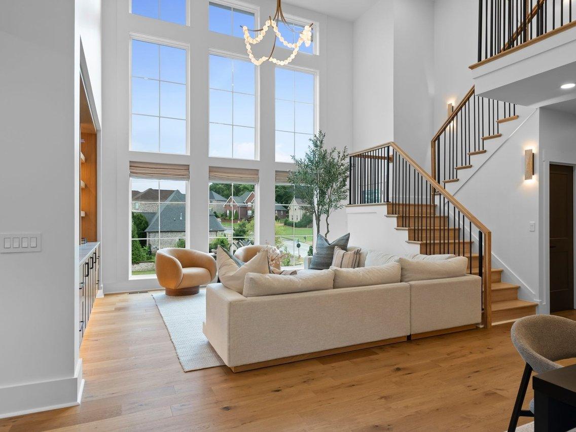 The living room toward the two-story wall of windows: two curved swivel chairs, an olive tree and Roman shades.