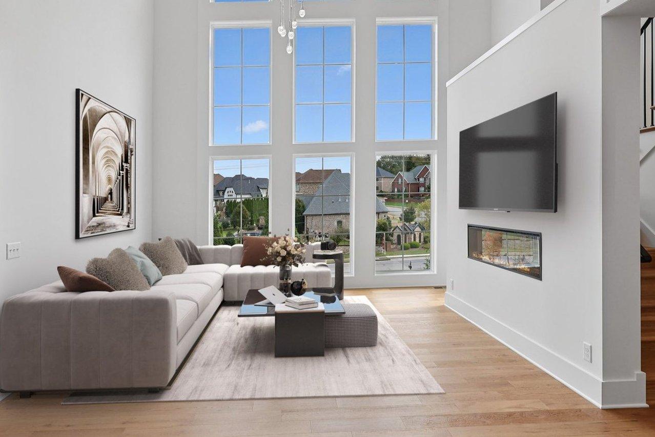 2025 photograph (before): Living Room, toward wall of windows from dining, with gray sectional, wall of windows, linear fireplace, TV