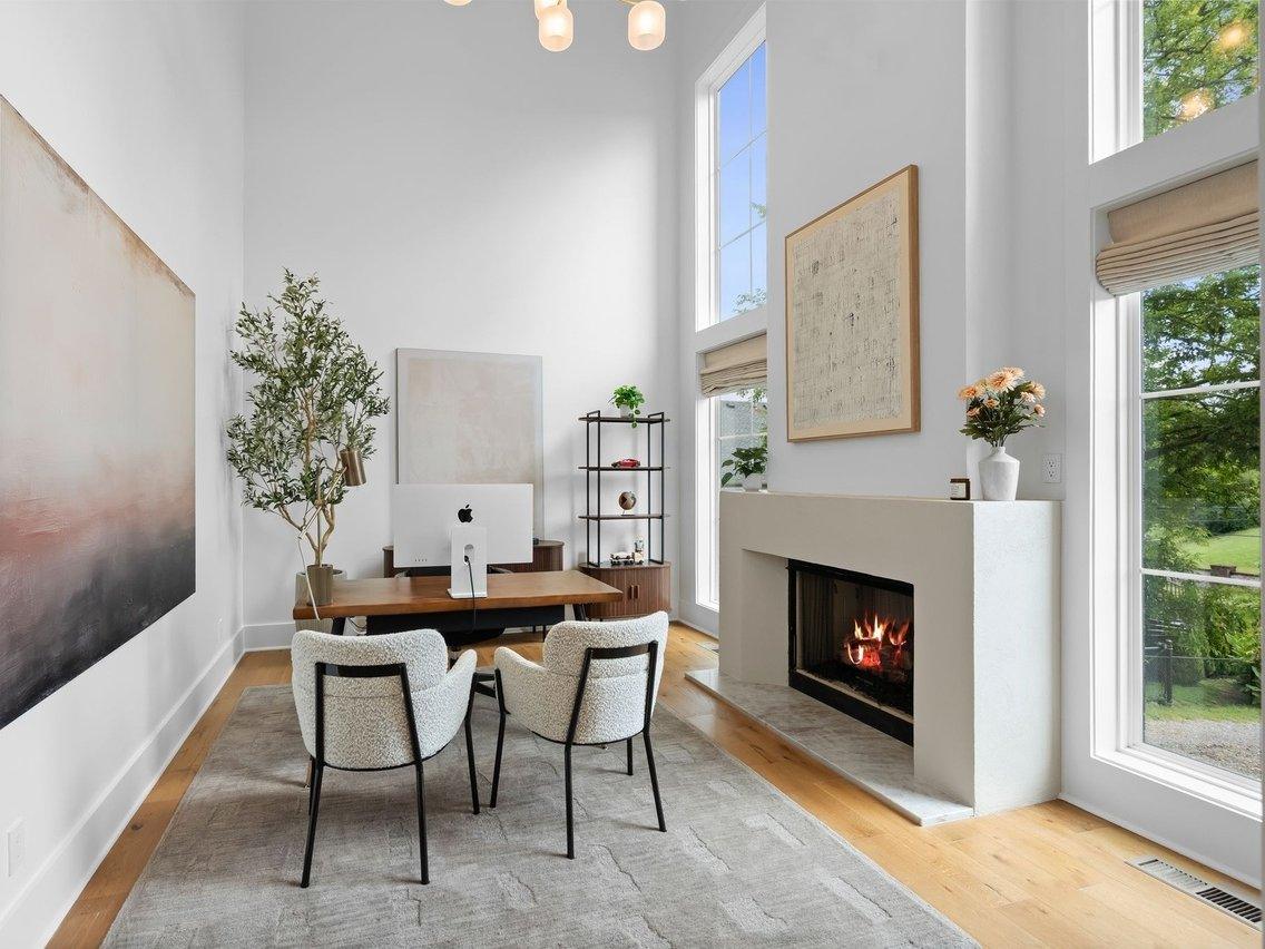 The office: a white plaster fireplace surround with a framed map above, a desk and two upholstered chairs on a gray rug.
