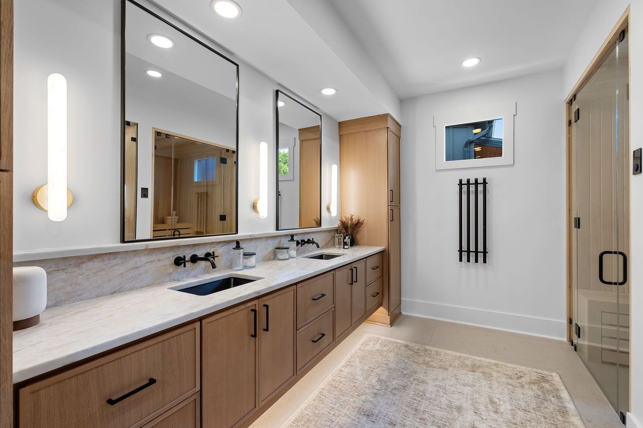 The double vanity: oak drawers, two undermount sinks, black wall-mounted faucets and frameless mirrors between vertical sconces.