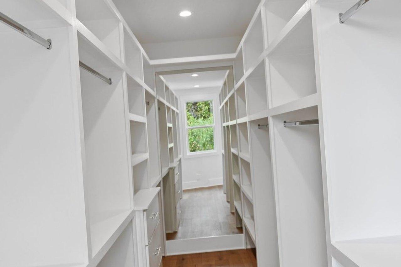 2025 photograph (before): Primary Closet, down aisle toward end mirror, with white built-in shelving, hanging rods, drawer stack, end mirror